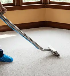 Steam carpet cleaning technician using a hot-water extraction wand on a residential carpet, wearing blue protective shoe covers Charleston, SC.