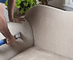 Professional upholstery cleaner deep-cleaning a fabric sofa with a handheld extraction tool and hose in Charleston, SC.
